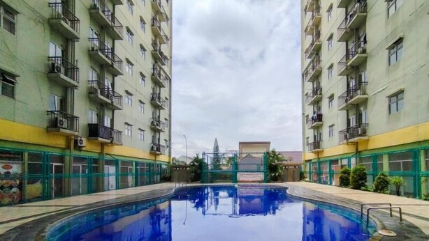 A swimming pool surrounded by high-rise residential buildings with balconies and air conditioning units. - Homey Studio At Apartment Suites @Metro (Bandung)