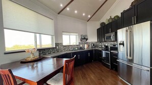 A modern kitchen with dark cabinetry, stainless steel appliances, and a wooden dining table. - Layin Low...Two Villas Offering 4 bedrooms, 2.5 baths on beautiful Staniel Cay (Staniel Cay)