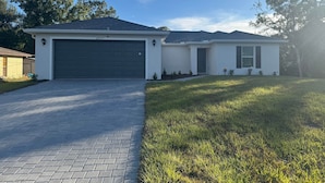 A single-story house with a dark garage door, a small front porch, and a well-maintained lawn. - Blue Mantle Charlotte Hideaway (Port Charlotte)