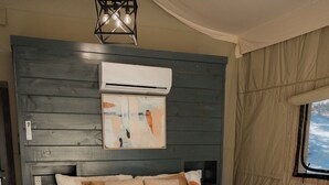 Un dormitorio con una cama grande, aire acondicionado de pared, lámpara colgante y ventana con cortinas.