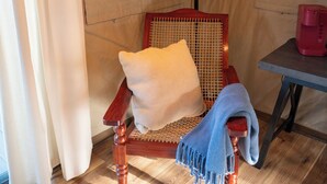 Una silla de madera con respaldo trenzado y cojín, una lámpara colgante y una mesa con un objeto rojo encima.