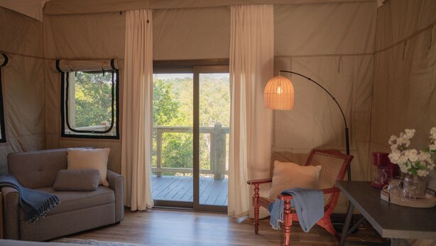 Una habitación acogedora con sofá, sillón, mesa con un jarrón de flores y vistas a una terraza de madera y vegetación.