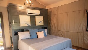 Un dormitorio con cama, un banco, un equipo de aire acondicionado y obras de arte en la pared.
