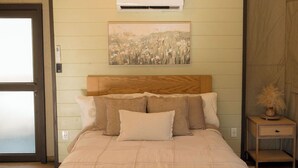 Une chambre dotée d’un grand lit, d’une tête de lit en bois, d’un appareil de climatisation, d’une table de chevet et d’une œuvre d’art accrochée au mur.