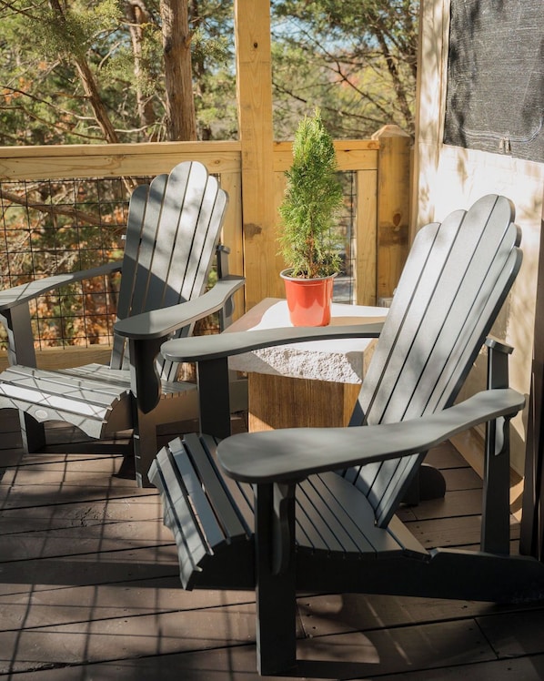 Une terrasse en bois, agrémentée de chaises Adirondack et d’une petite table, le tout entouré d’arbres.