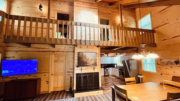 A wooden cabin interior with a dining area, kitchen, and a balcony.