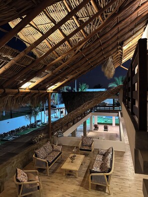 Un espace de détente extérieur aménagé avec des meubles en osier, un toit de chaume et une vue sur une piscine.