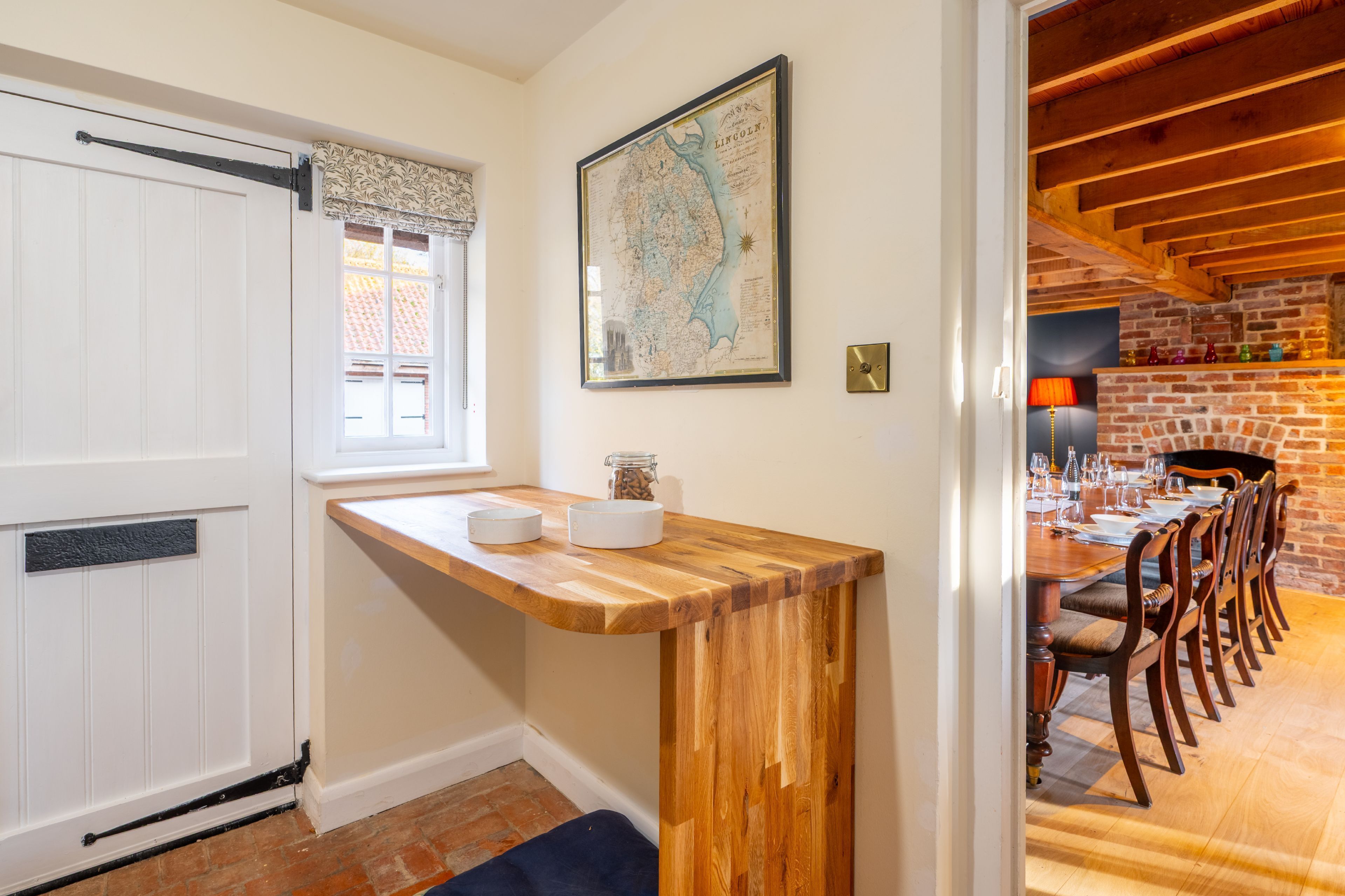 A dining area with a wooden table set for four, a brick fireplace, and a map on the wall.