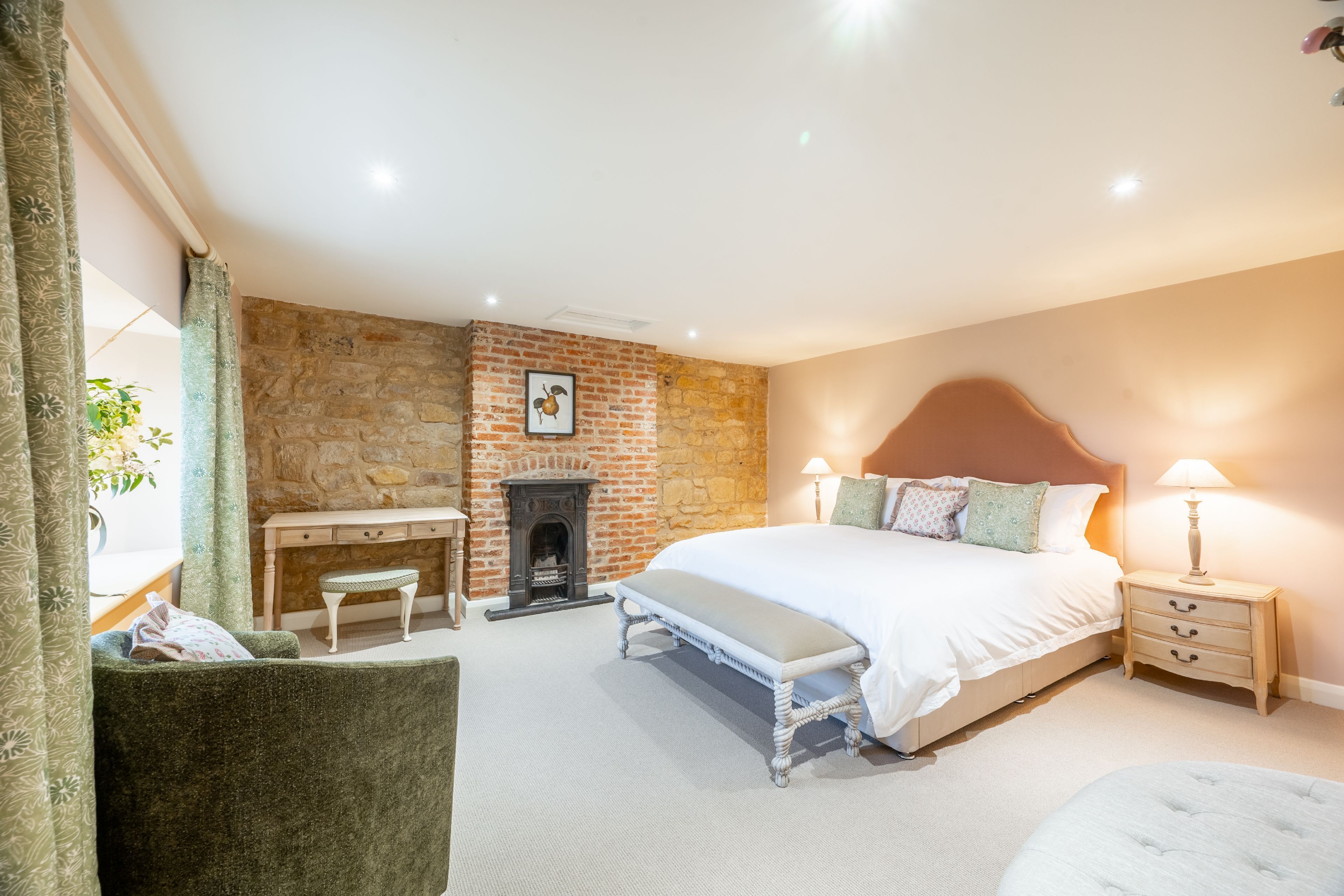 A bedroom with a brick wall, a fireplace, a bed with a headboard, a desk, a chair, and a bench.