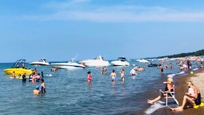 Una playa concurrida, gente nadando y barcos en el agua.