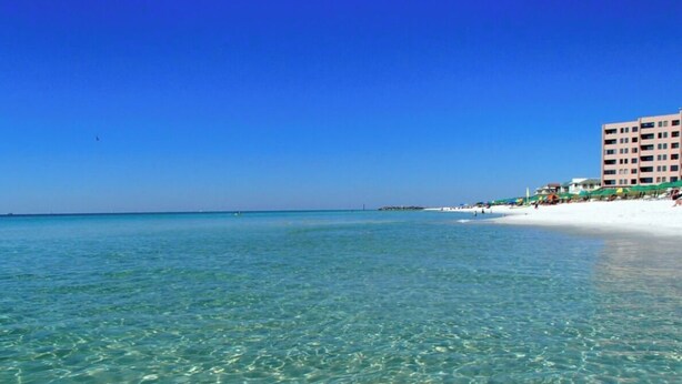 Una playa con agua turquesa cristalina, arena blanca y un edificio con varios balcones.