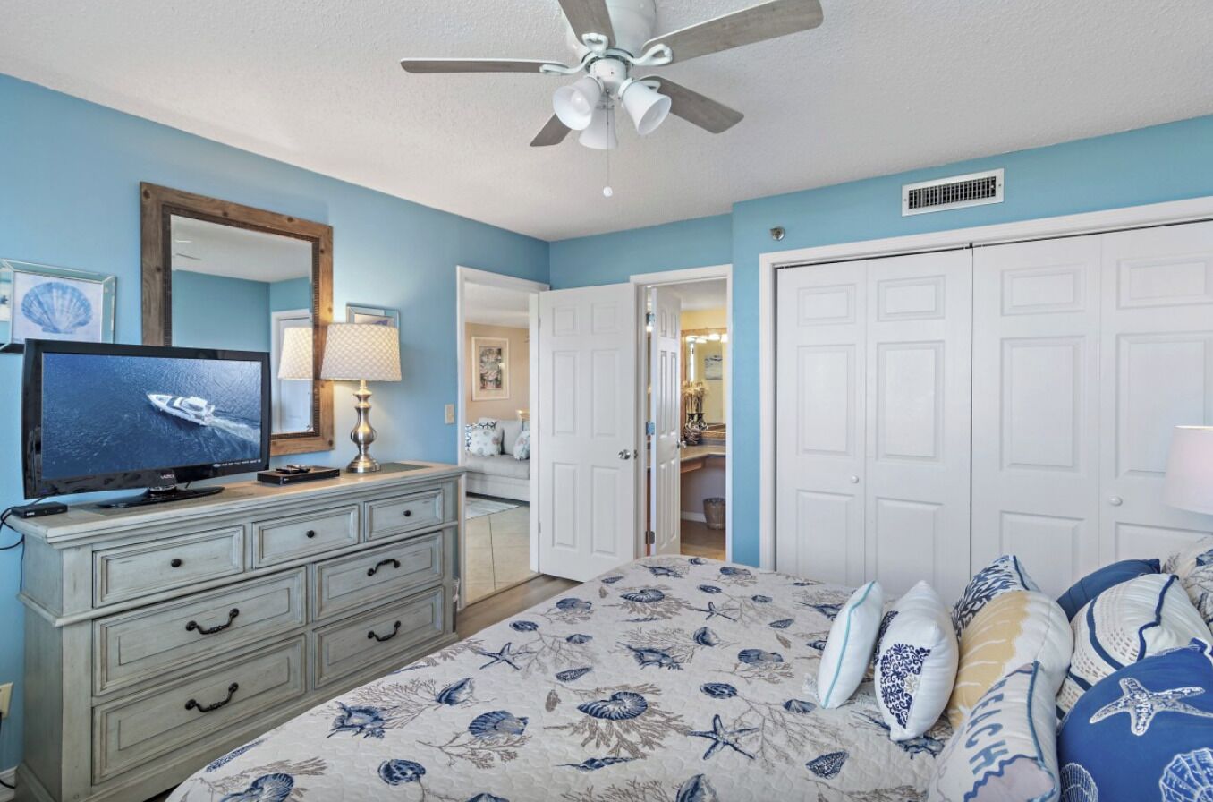 A bedroom with a bed, dresser, television, and a ceiling fan.