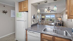 Una cocina con armarios de madera, un refrigerador blanco, lavavajillas, encimera de granito, pileta doble y luces colgantes.