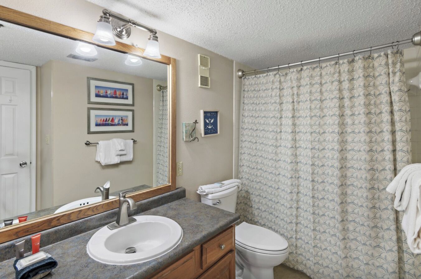 A bathroom with a sink, mirror, toilet, and shower curtain.
