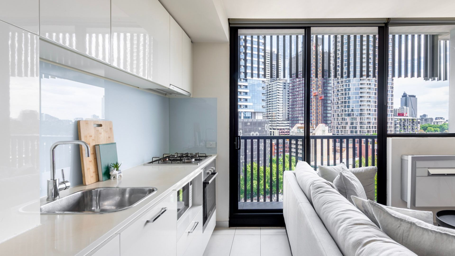 A modern kitchen with a large window, a balcony, and a view of city buildings.