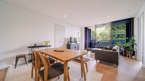 A modern living room with a wooden dining table, grey sofa, and a balcony with plants.
