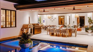 Et rummeligt indendørs område med pool, grillstation og spiseplads med flere borde og stole.