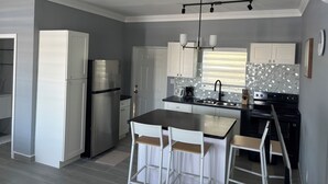 A modern kitchen with white cabinetry, a stainless steel refrigerator, a black stove, and a bar stool. - Brand New Apartment in George (George Town)