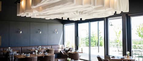 An indoor dining area with tables and chairs, large windows, and a ceiling with hanging fabric.
