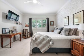 A bedroom with a bed, a desk, a chair, a TV, and a window with curtains. - Coorabin | Pet-Friendly 4BR near Orange CBD (Orange)