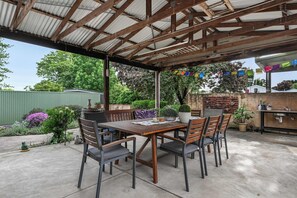 An outdoor patio with a wooden table and chairs, surrounded by greenery and a brick wall. - Coorabin | Pet-Friendly 4BR near Orange CBD (Orange)