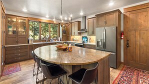 Una cocina con armarios de madera, una isla grande con taburetes de bar, electrodomésticos de acero inoxidable y una araña.