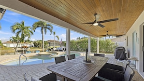 Un patio couvert avec une piscine, du mobilier d’extérieur et un ventilateur de plafond.