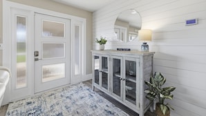 Un couloir avec une porte blanche, un miroir, une armoire aux portes vitrées, une lampe et une plante en pot.