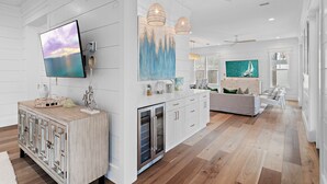 A spacious living area with a large flat-screen TV, wooden cabinets, and a modern kitchen. - 6BR 30A Oasis • Pool, Golf Cart & Bikes (Seagrove Beach)