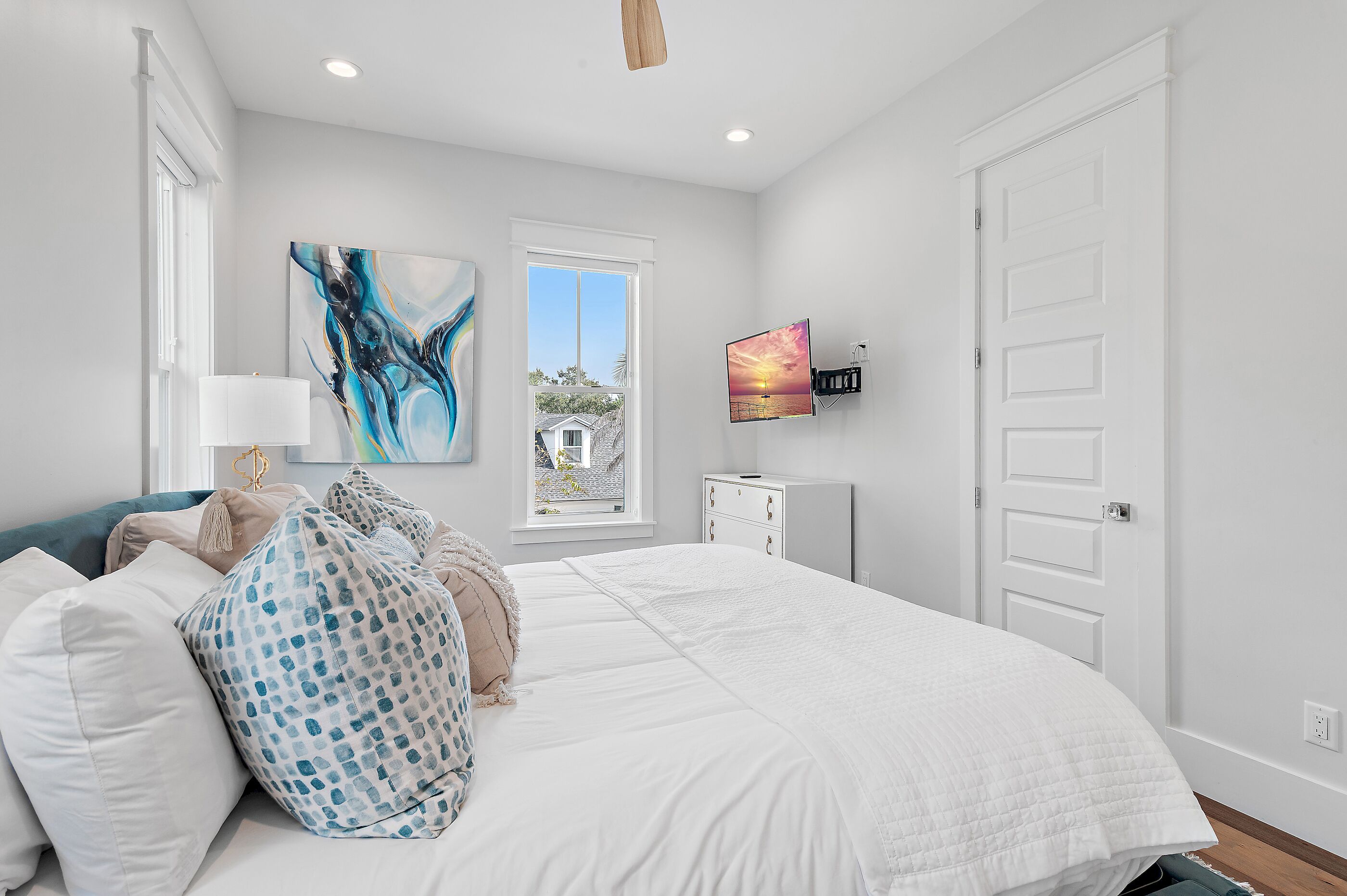 A bedroom with a large bed, a TV mounted on the wall, and a window with a view of the outside.