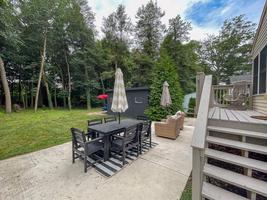 Een terras met een tafel en stoelen, omgeven door bomen en een tuinhuis.