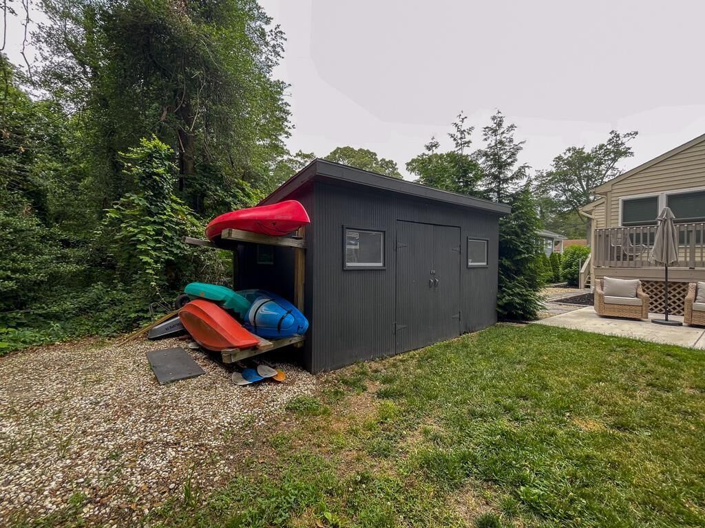 A small, dark-colored shed with a red roof, a door, and windows.