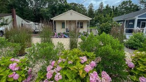 Een klein huis met een veranda, omringd door een tuin vol roze hortensia’s.