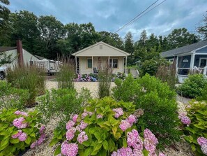 A small house with a porch, surrounded by a garden with pink hydrangeas. - The Salt Box Beach House. 2 Blocks to Beach. (Villas)