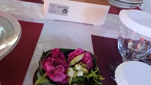 A dining table set with plates, glasses, and cutlery, a vase with flowers, and a decorative box. - GRHA PAWITRA TROWULAN (Bejijong)