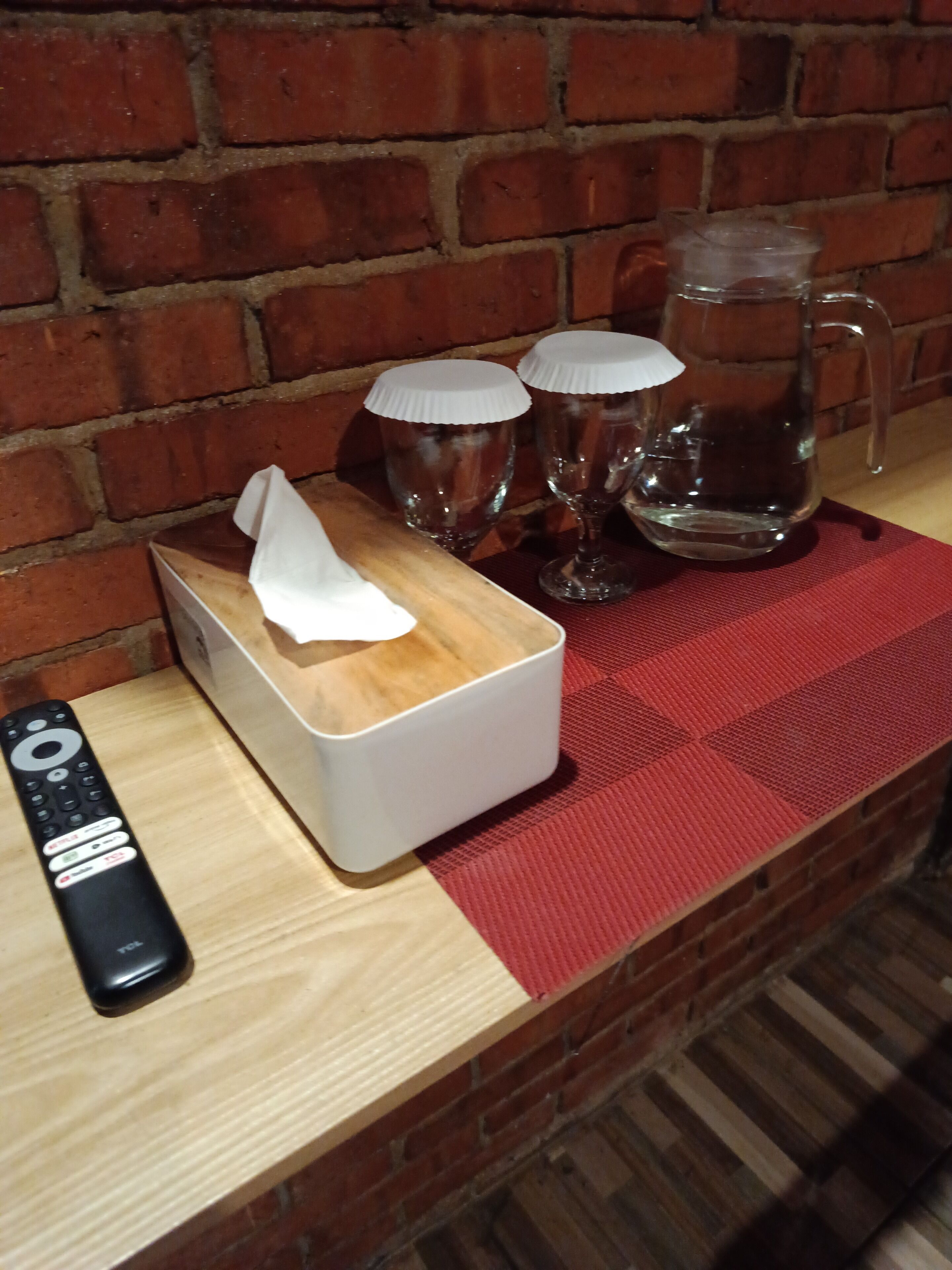 A wooden table with a remote control, a tissue box, and two glasses with lids.