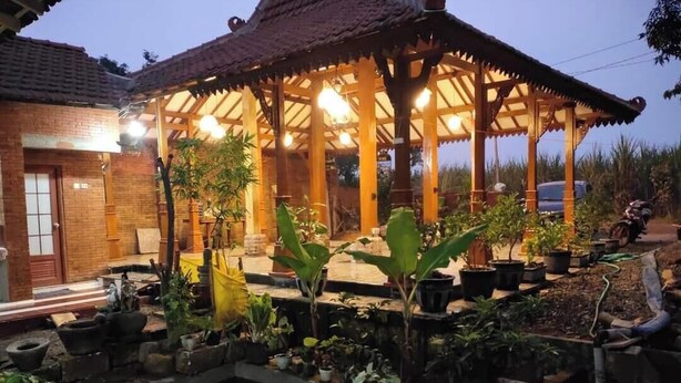 A wooden gazebo with a tiled roof, surrounded by potted plants and a brick building. - GRHA PAWITRA TROWULAN (Bejijong)