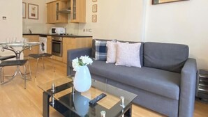 Uma sala de estar moderna com um sofá cinzento, uma mesa de centro de vidro e uma área de jantar com mesa e cadeiras de vidro.