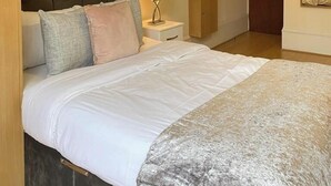 Quarto com cama, mesa de cabeceira, luminária, armário de madeira e espelho na parede.