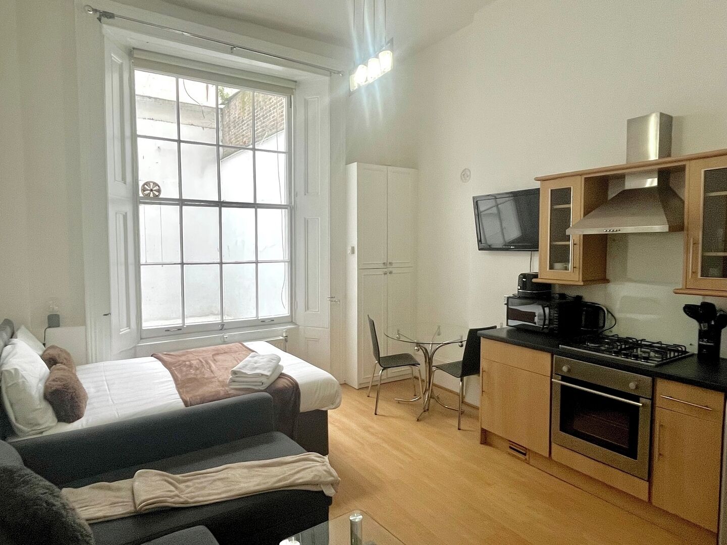 Una habitación funcional con cama, sofá, una pequeña mesa de comedor, televisor y kitchenette.
