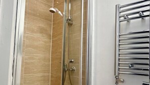 Eine begegnete Duschkabine mit Handbrause und Duschschlauch, ein Handtuchhalter und ein Toilettenpapierhalter an der Wand.