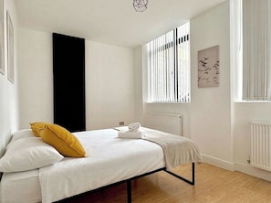Ein Schlafzimmer mit Bett, Heizkörper, Fenster mit Jalousien und einem Wandbild.