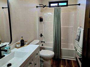 A bathroom with a white sink, toilet, and shower area. There are toiletries on the sink and a towel hanging on the shower door. - The Riverlight 3 Bedroom Townhouse (Helena)