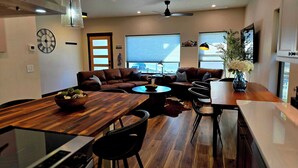 Ein modernes Wohnzimmer mit einem Holzesstisch, Ledersofas und einem großen Fenster mit Jalousien.