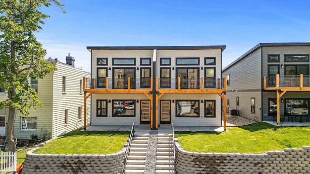 Ein modernes, zweistöckiges Haus mit Balkon, Vordergarten und einer Steinmauer.