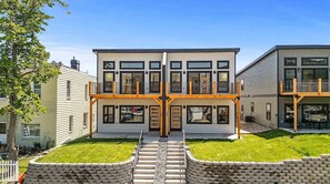 A modern two-story house with a balcony, a front yard, and a stone retaining wall. - The Riverlight 3 Bedroom Townhouse (Helena)