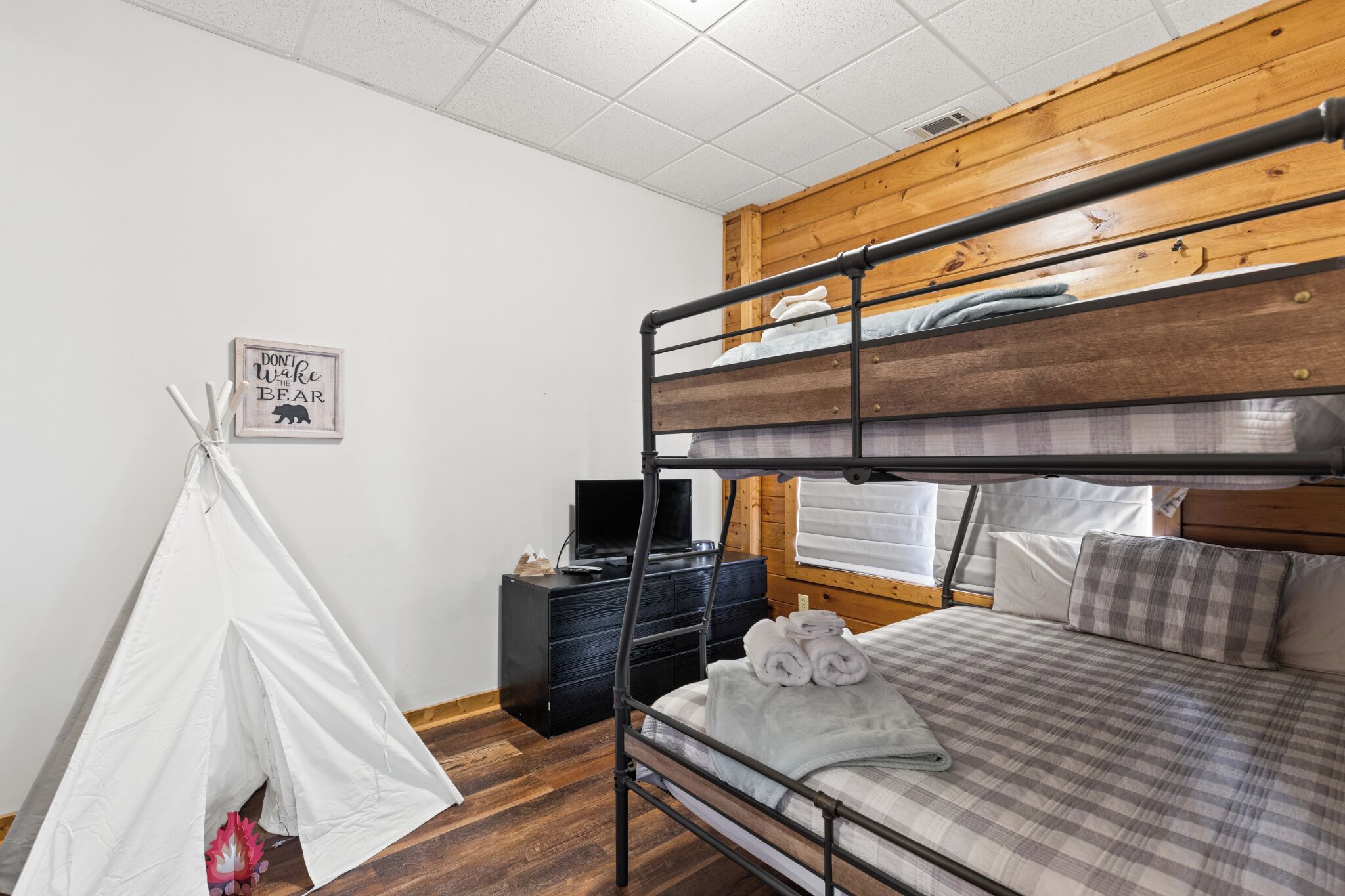 A bunk bed room with a wooden headboard, a white teepee, a black dresser, and a framed sign on the wall.
