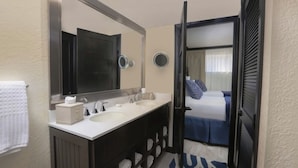 A hotel bathroom with a double sink vanity, a large mirror, and a view into a bedroom with a bed and curtains. - Westgate Lake Resort & Spa (Orlando)