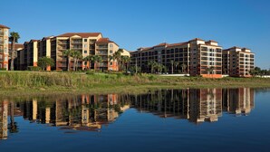 A multi-story hotel with balconies, a reflection in the water, and palm trees. - Westgate Lake Resort & Spa (Orlando)