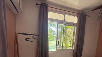 Una habitación pequeña y limpia con una cama, un ventanal con cortinas, un radiador y una mesita con hervidor.